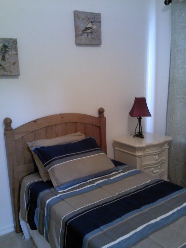 A cozy bedroom with a single bed, striped bedding, and a nightstand featuring a red lamp.
