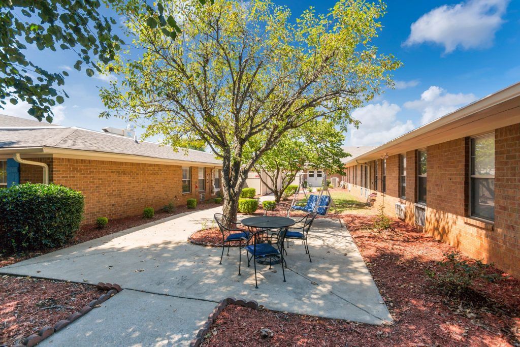 A sunny courtyard with outdoor seating and a tree between two buildings.