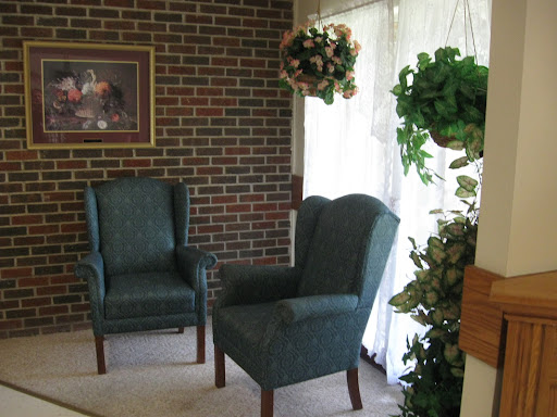A cozy seating area featuring two upholstered chairs and decorative plants against a brick wall.