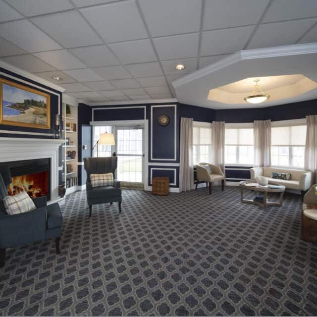 A cozy lobby with a fireplace and comfortable seating areas, accented by large windows and artwork.