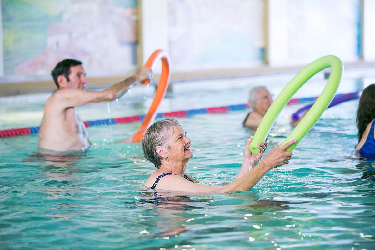 Seniors engaging in a water aerobics class using pool noodles.