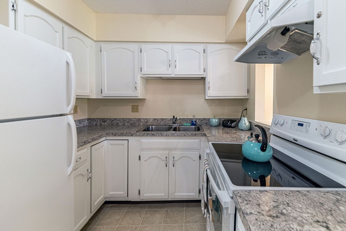 A cozy kitchen with white cabinets, granite countertops, and a turquoise teapot on the stove.