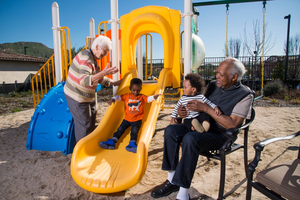 A joyful moment at the playground with children on the slide and grandparents watching.
