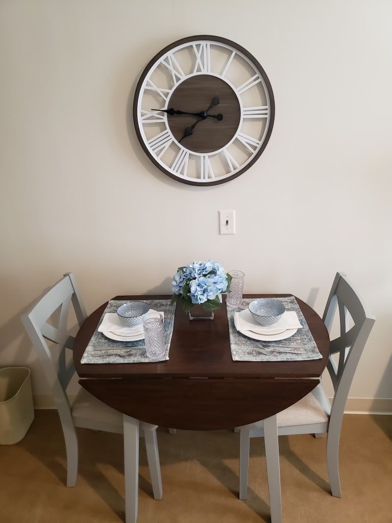 A cozy dining setup with a round table for two, complete with place settings and a decorative clock on the wall.