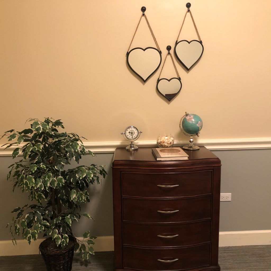 A cozy interior setup featuring a dresser adorned with decorative items, a plant, and heart-shaped mirrors on the wall.
