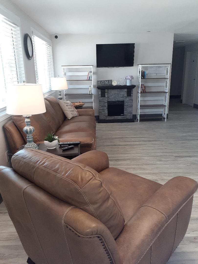 A cozy living room with brown leather sofas, a wall-mounted TV, and ambient lighting.