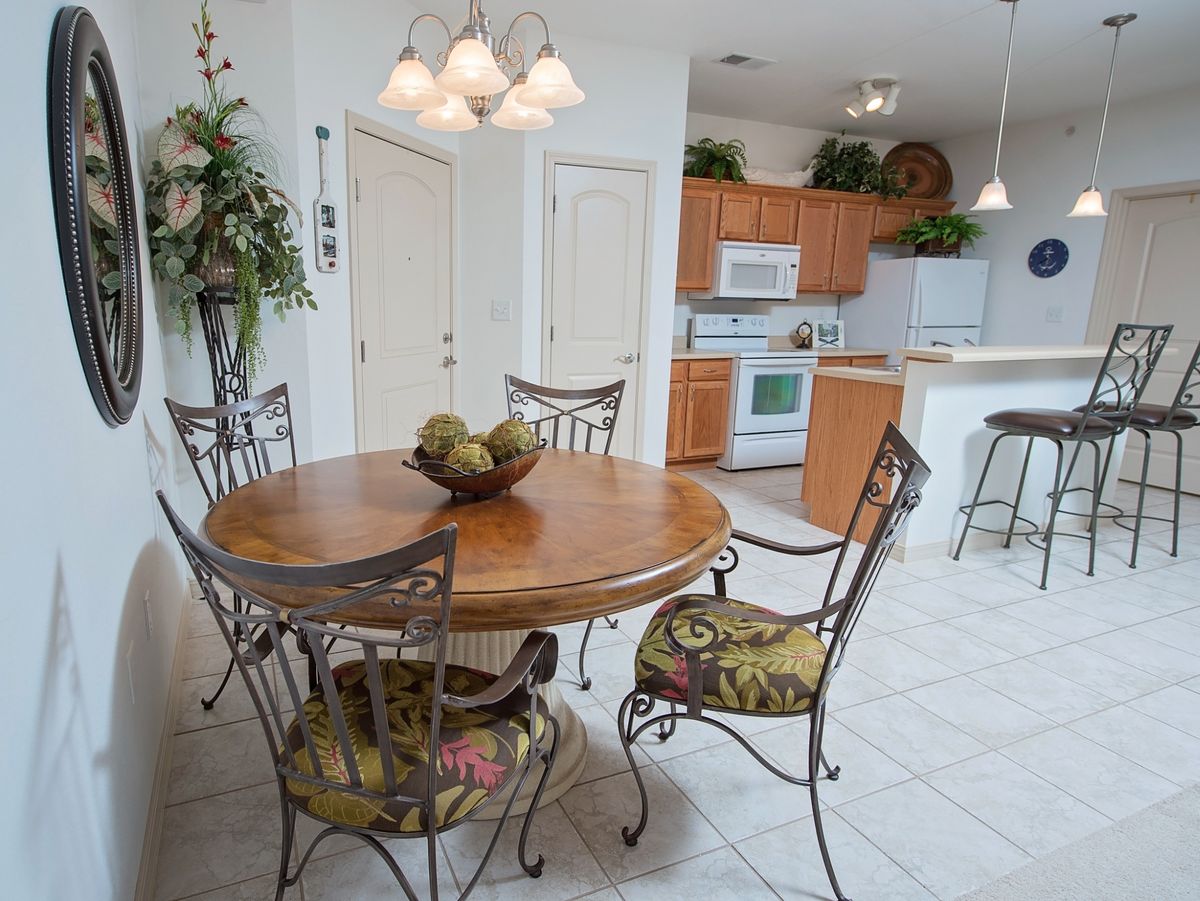 A modern kitchen and dining area featuring a round wooden table with four chairs, surrounded by white cabinetry and indoor plants.