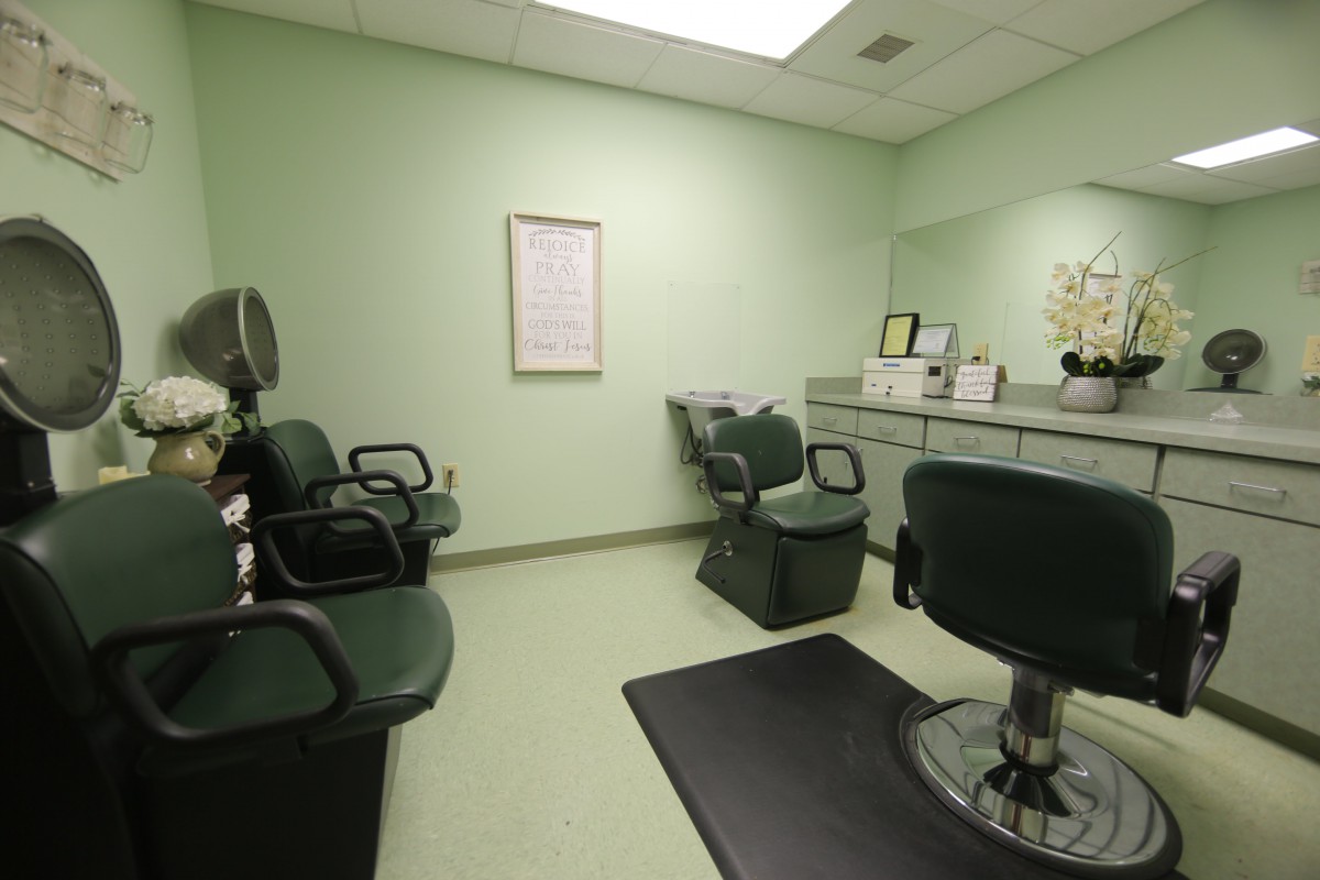 An empty hair salon with green walls and several chairs for clients.