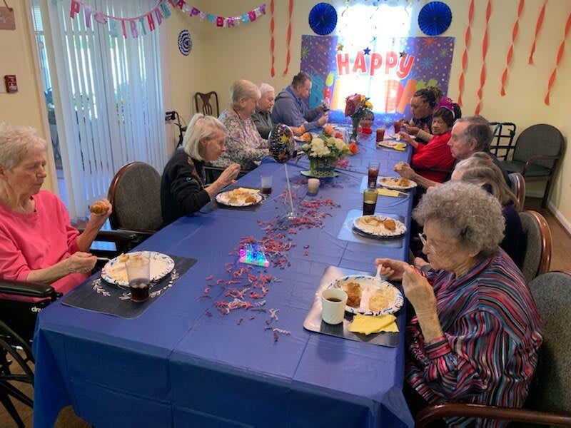 A group of elderly people enjoying a festive birthday celebration with food and decorations.