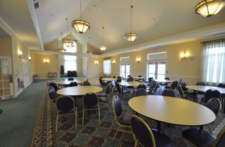 A spacious conference room with round tables and chairs, well-lit by overhead lighting and natural light from windows.