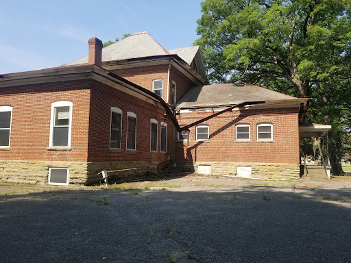 An abandoned brick house showing signs of wear and neglect, surrounded by greenery.