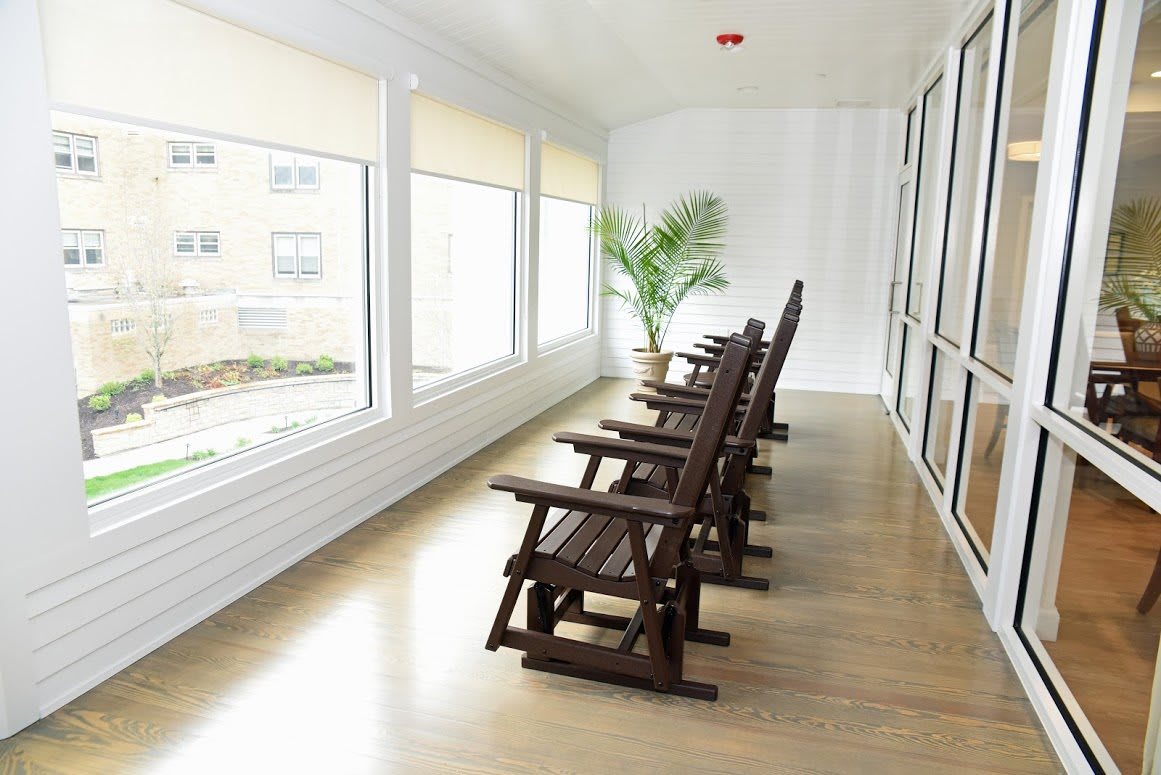 A serene sunroom with wooden rocking chairs aligned by large windows, allowing abundant natural light to fill the space.