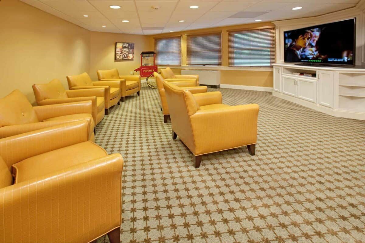 A bright and comfortable waiting room with yellow armchairs, carpeting, and a wall-mounted television.