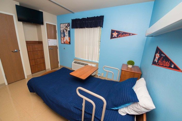 A cozy room with a hospital bed, blue walls, and sports-themed decor including a pennant flag and a poster.