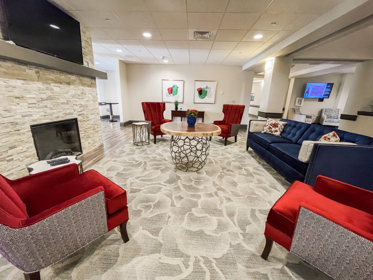 A modern living room with red chairs and a blue sofa arranged around a fireplace.