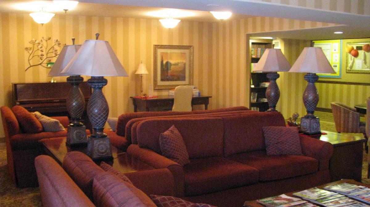 A cozy living room with sofas, lamps, and a desk in the background.