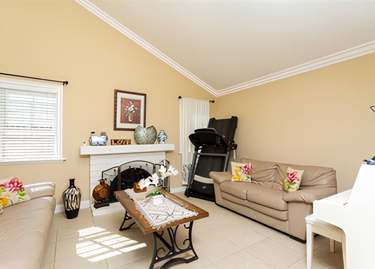 A cozy living room with a beige color scheme, featuring a sofa, coffee table, treadmill, and decorated fireplace.