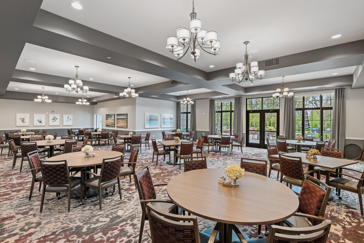 A spacious dining room with multiple round tables, chairs, and elegant chandeliers.