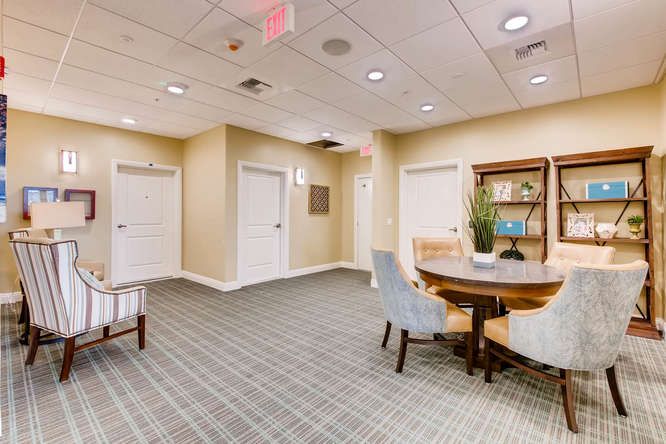 A modern waiting area featuring a round table with chairs, a plant centerpiece, and a bookshelf in the background.