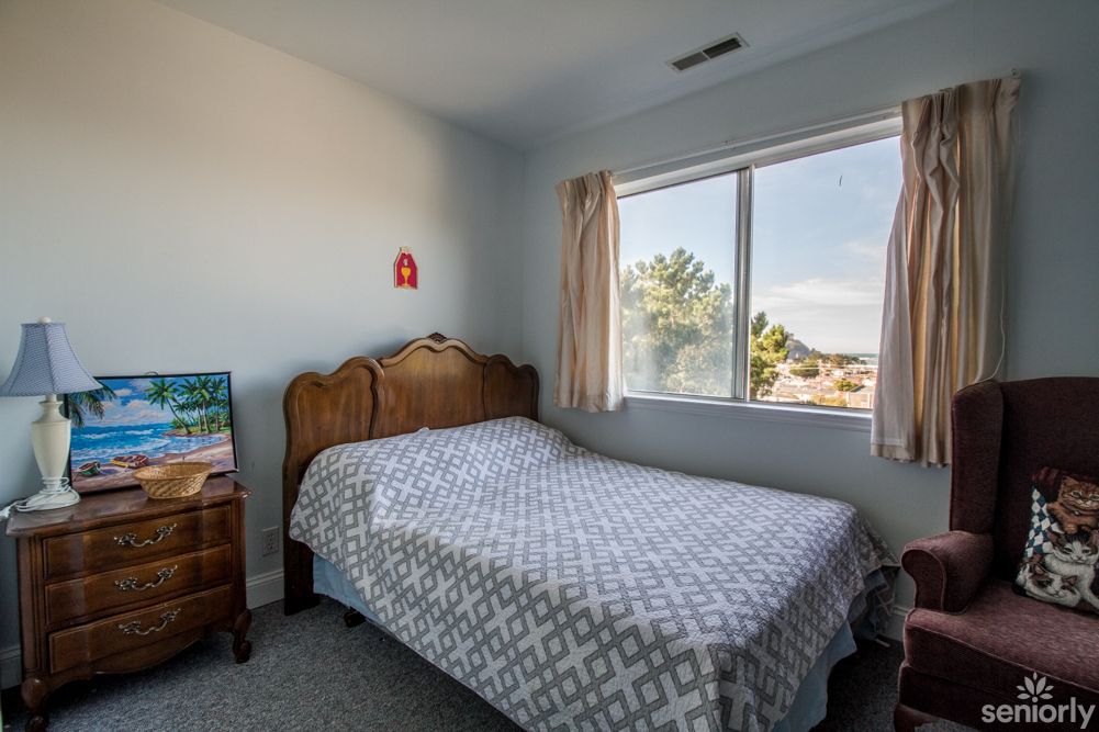 A cozy bedroom with a neatly made bed and a large window letting in natural light.