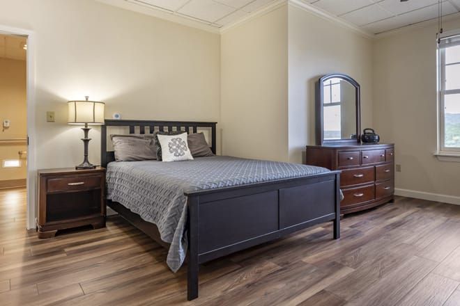 A cozy bedroom with a modern bed and matching furniture, featuring a nightstand, dresser, and mirror on wooden flooring.
