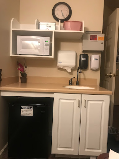 A small kitchenette area featuring a microwave, sink, and refrigerator with shelving for storage.