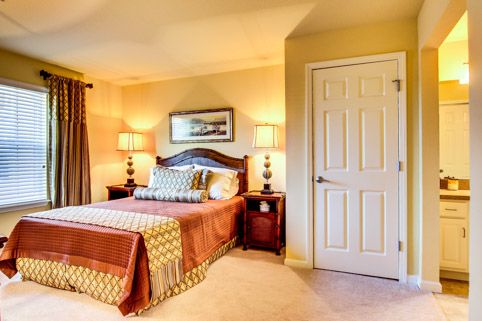 A cozy and well-decorated bedroom featuring a bed with pillows, nightstands with lamps, and a door in the background.