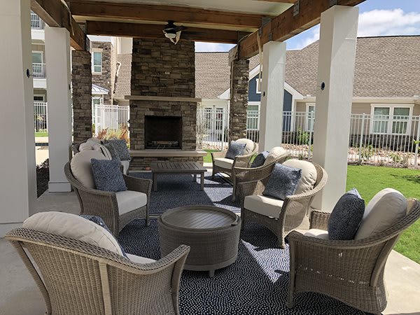 A cozy outdoor patio setup with comfortable wicker chairs and a fireplace under a covered area.