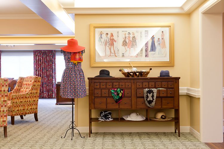 A stylish interior with vintage decor, featuring a mannequin wearing a dress and hat, alongside an ornate piece of furniture adorned with accessories and artwork above.