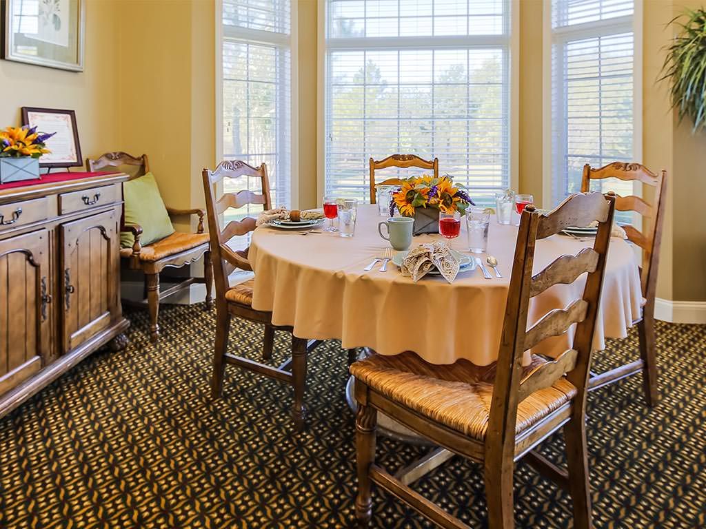 A cozy dining room with a round table set for a meal, surrounded by wooden chairs and large windows letting in natural light.