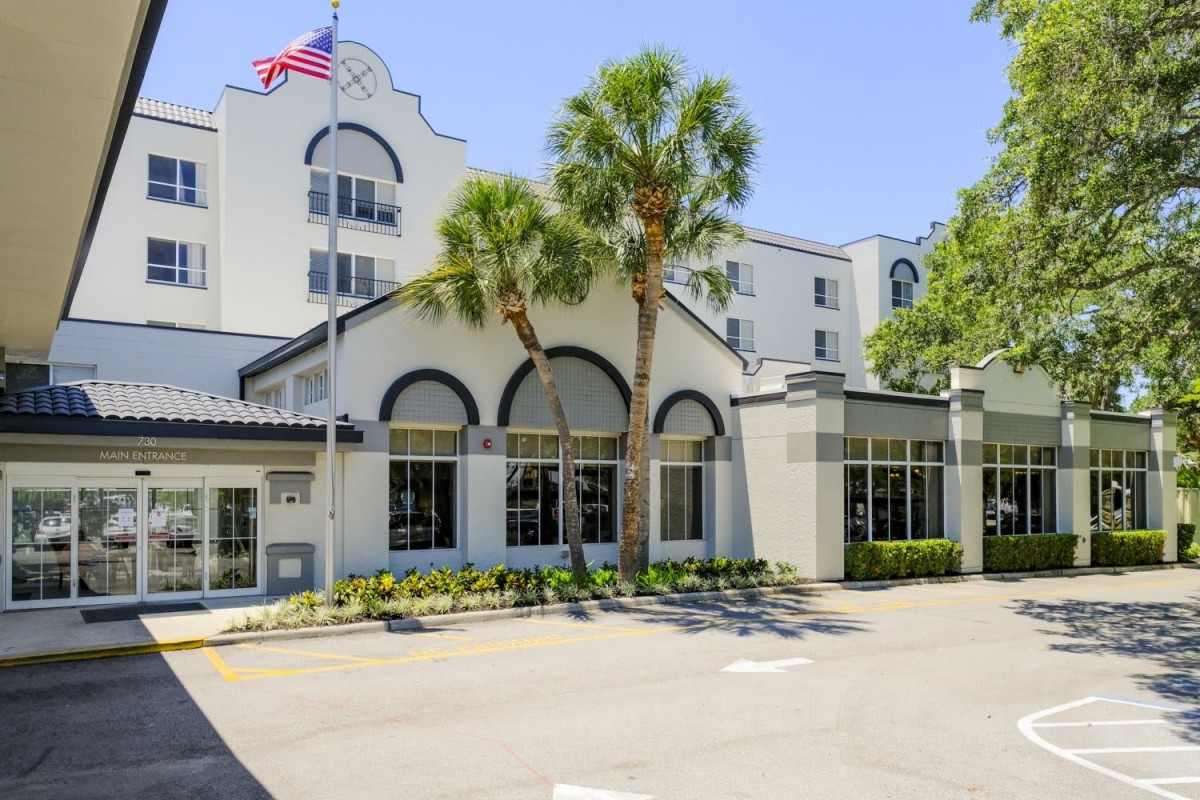 A hotel building with palm trees and an American flag.