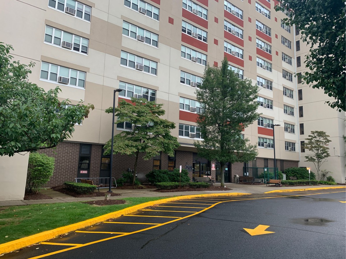 View of a high-rise apartment building with trees and a parking lot in the foreground.