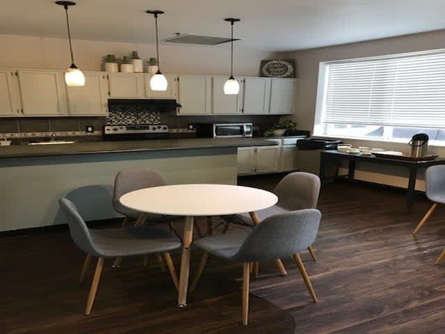 A modern kitchen and dining area with a round table and chairs, featuring pendant lights and wood flooring.