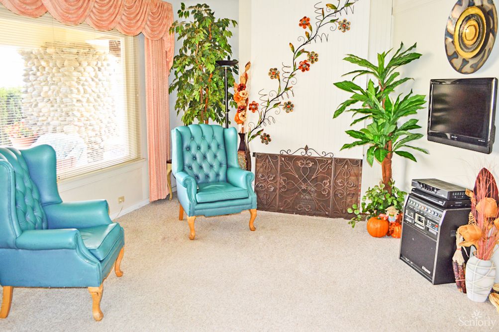 A cozy living room with teal chairs, lush plants, and floral wall decor.