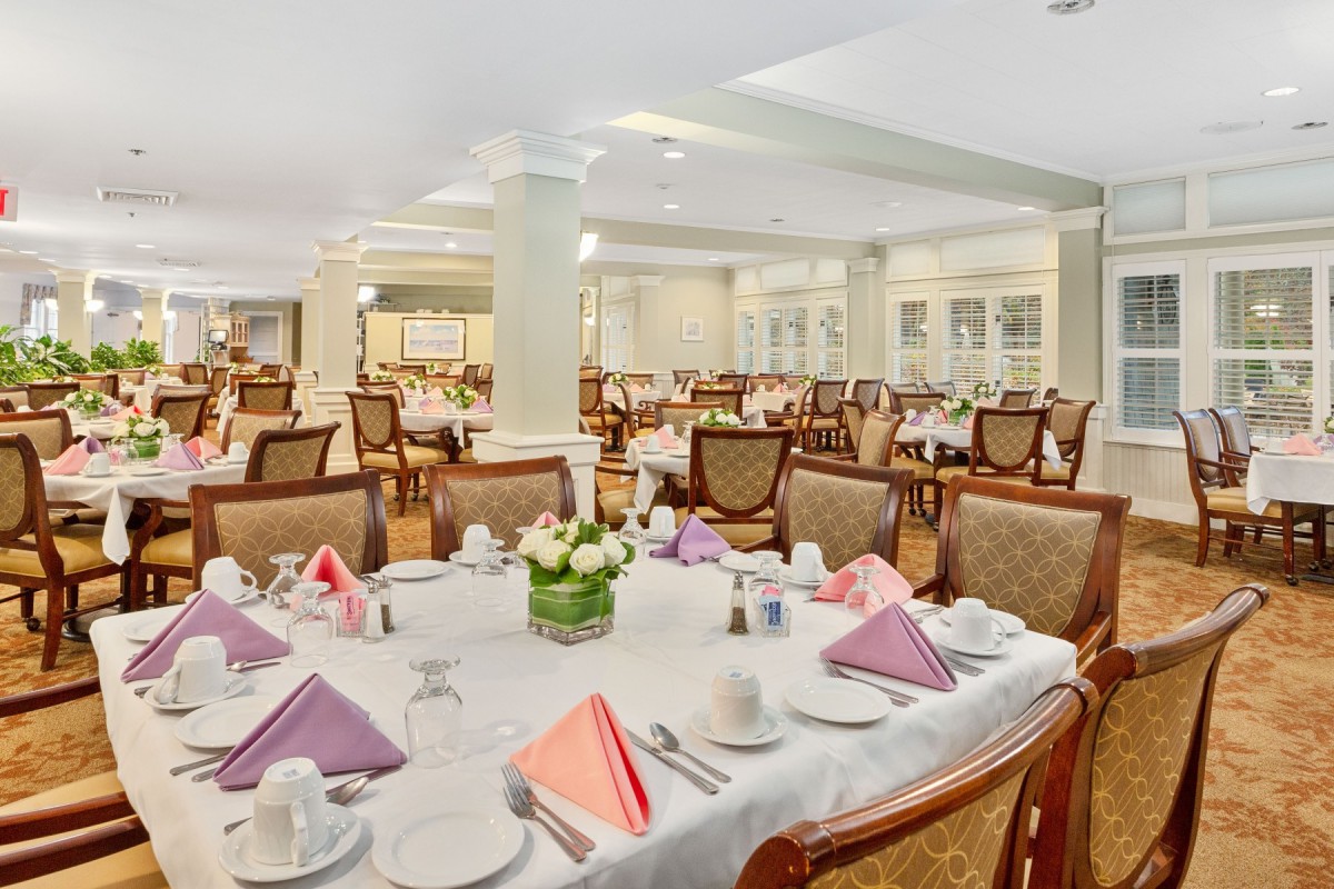 An elegant dining room with tables set for guests, featuring folded napkins and floral centerpieces.