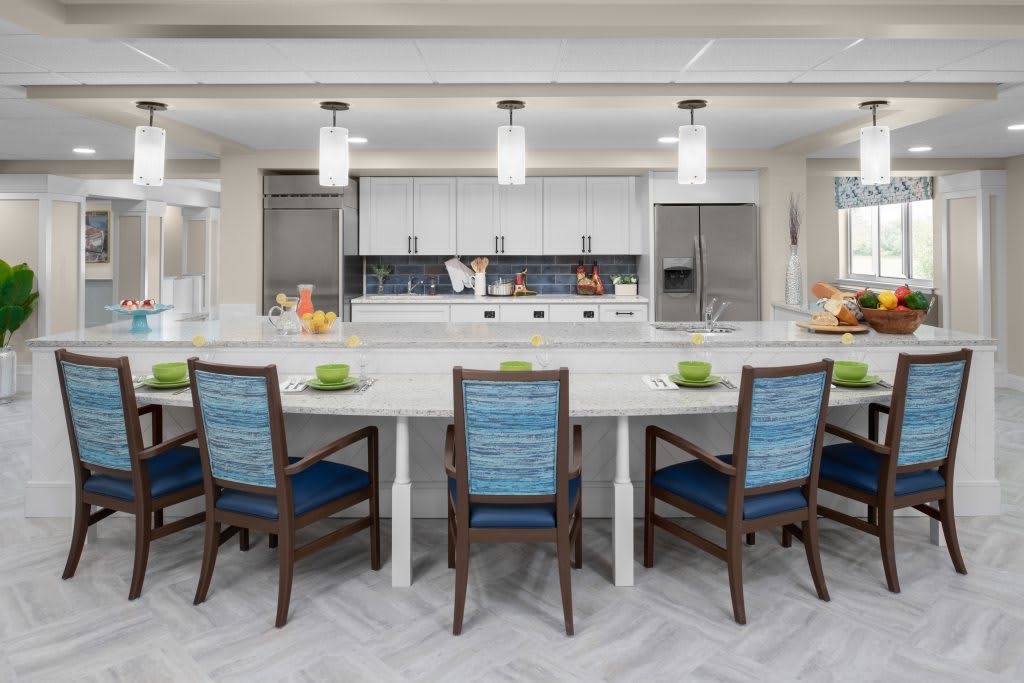 A modern kitchen with a long island, stylish chairs, and elegant lighting fixtures.