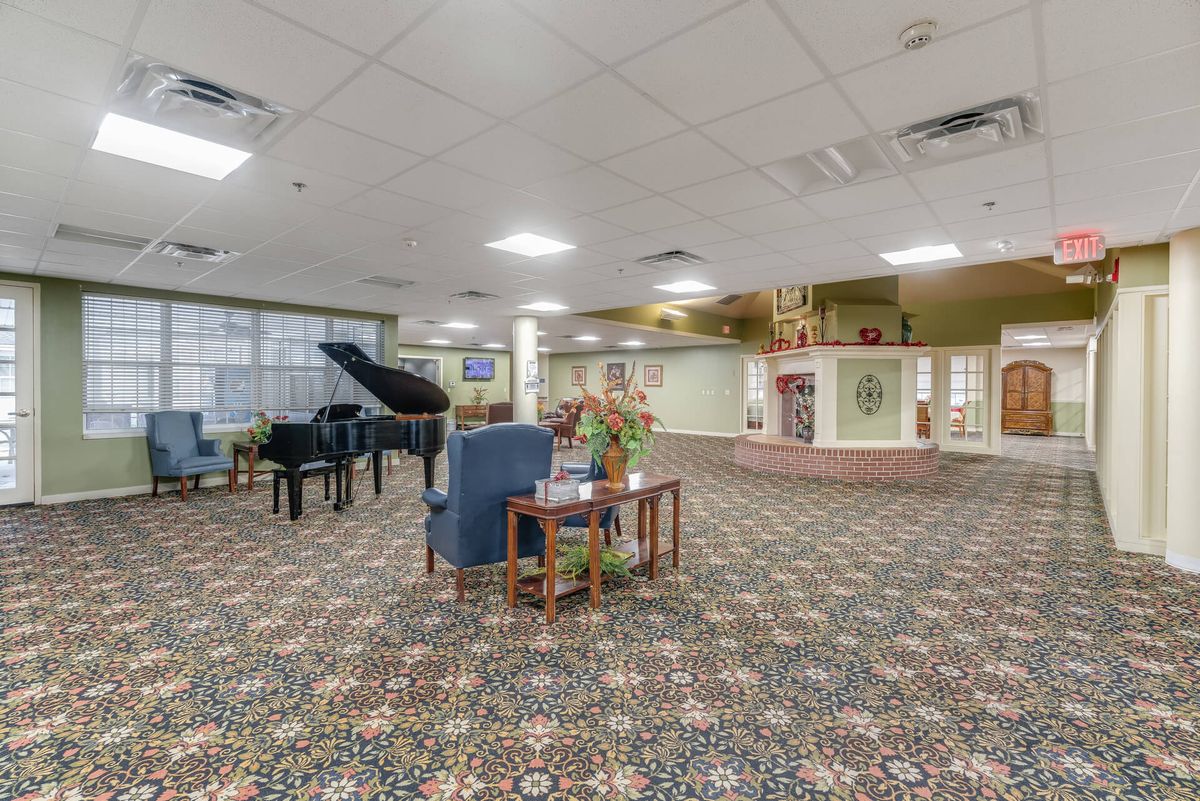 A spacious lobby area featuring a grand piano, comfortable seating, and decorative floral arrangements on a patterned carpet.
