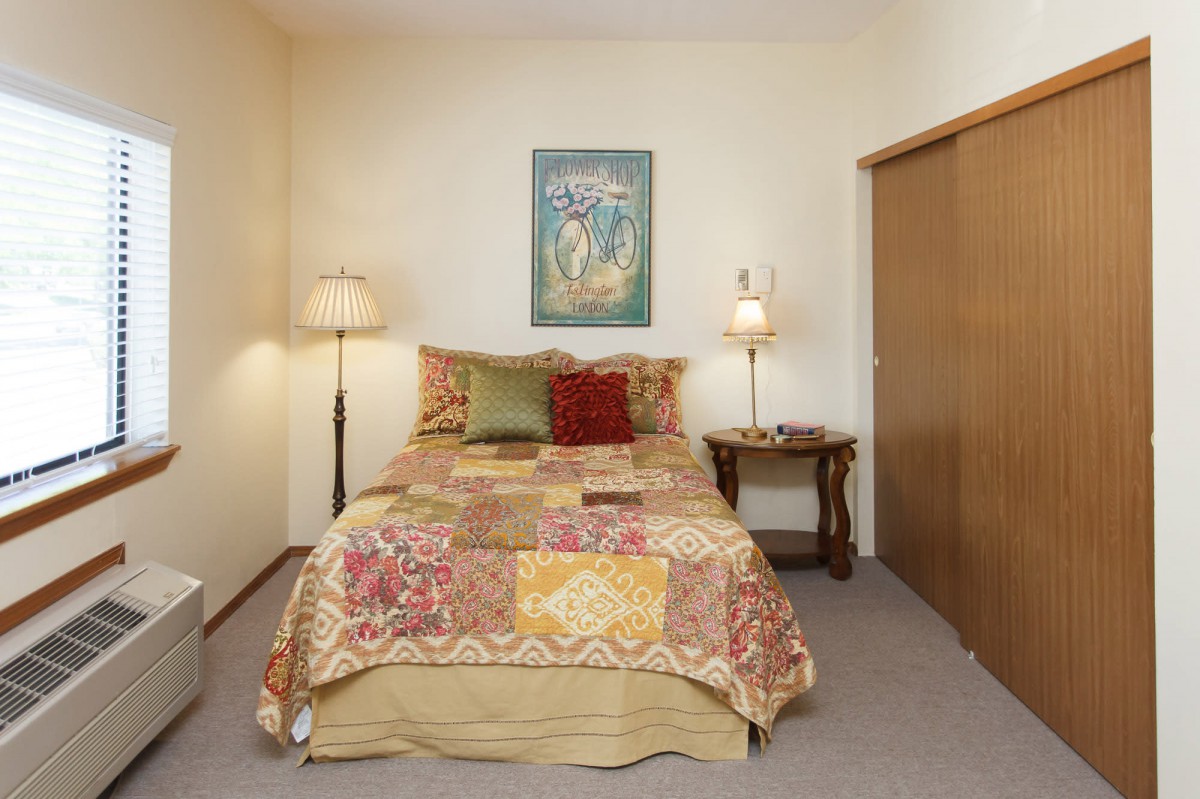 A cozy bedroom with a quilted bed, two lamps, and simple decor.