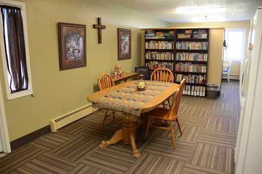 A cozy dining area featuring a wooden table surrounded by chairs, decorated with a tablecloth and accompanied by a bookshelf filled with various items.