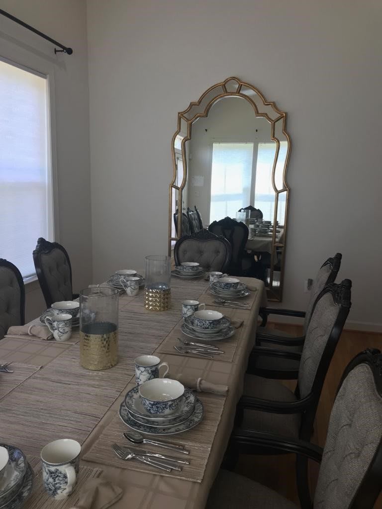 A dining room with an elegantly set table, featuring a large mirror and upholstered chairs.