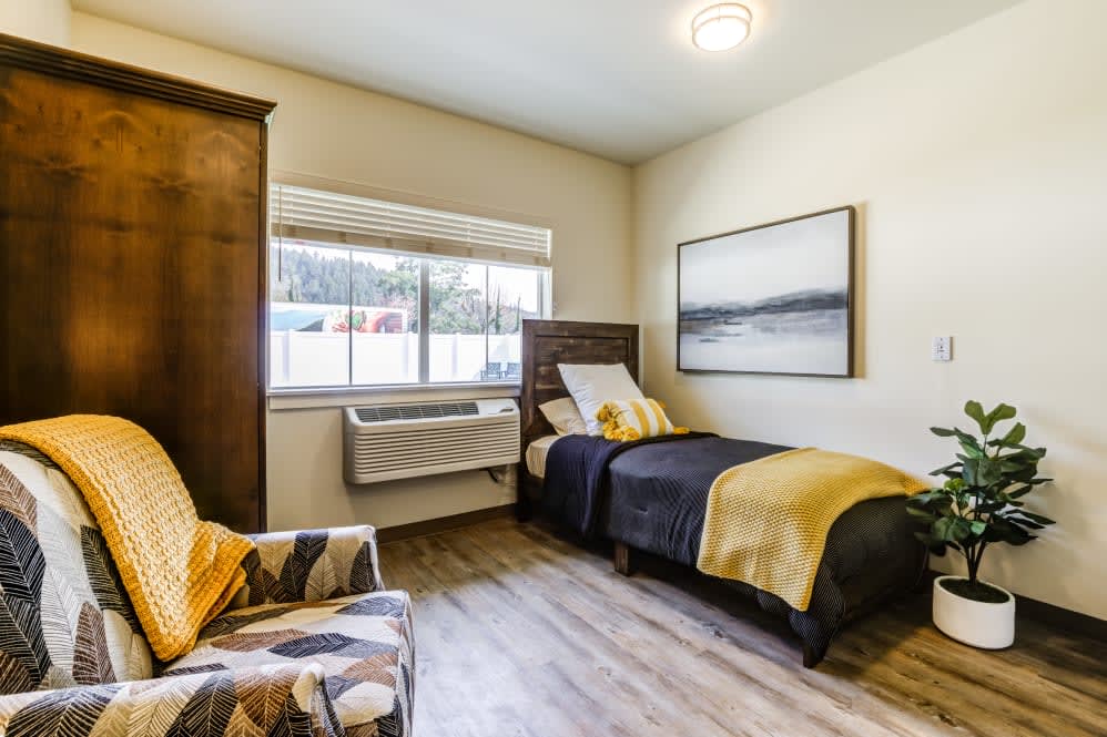 A cozy bedroom with a single bed, artwork on the wall, and a window providing natural light.