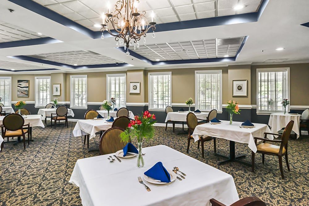 An elegant restaurant dining room featuring neatly set tables, a chandelier, and decorative flowers.