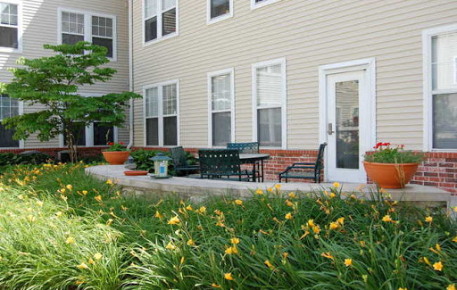 A serene outdoor patio area with seating and blooming flowers in front of an apartment building.