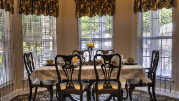 A cozy dining room with a beautifully set table and elegant chairs in front of large windows.