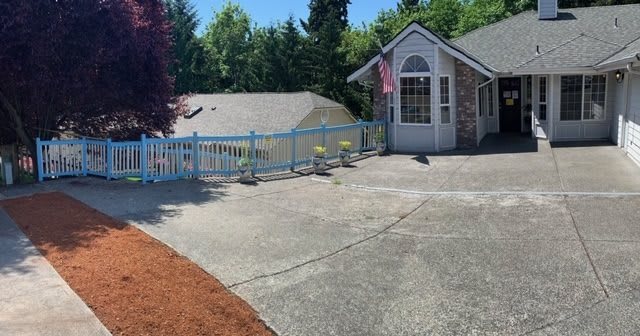 A suburban house with a driveway and fenced yard, surrounded by trees.