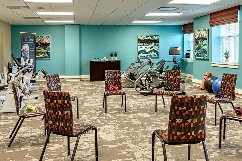 A brightly lit meeting room with patterned chairs arranged in a circle and exercise bikes against the wall.