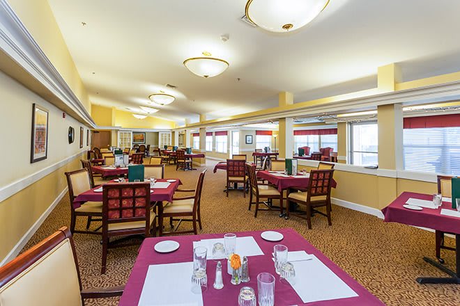 A spacious dining area with neatly arranged tables and chairs, featuring overhead lighting and a carpeted floor.