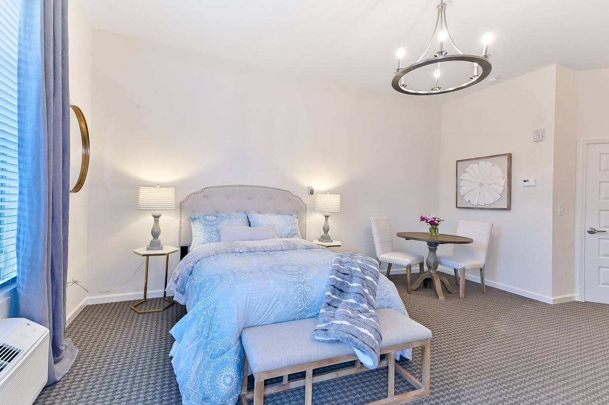 A modern bedroom featuring a cozy bed with soft bedding, elegant lamps, a stylish chandelier, and a small round table with chairs.