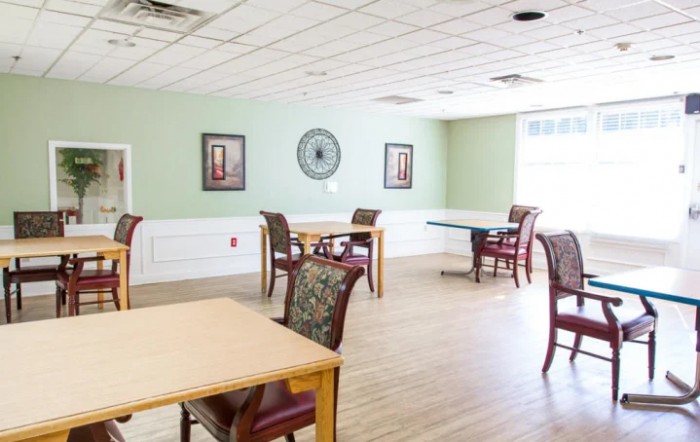 A bright and spacious dining area with several tables and chairs, featuring green walls, a clock, and wall art.