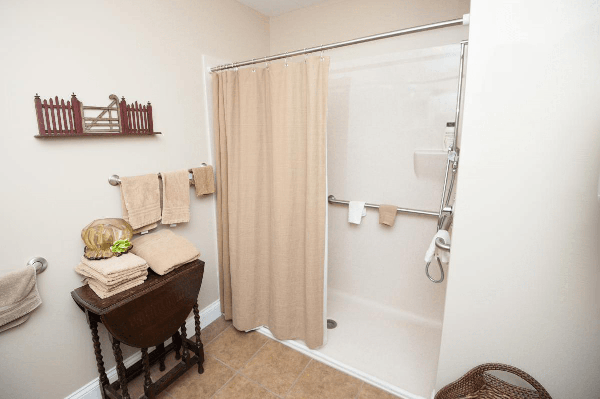 A tidy bathroom featuring a shower with a beige curtain, neatly arranged towels, and a small table with decor.